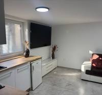 Wohnzimmer in einem Einfamilienhaus mit weißer Küchenzeile und dunkelbraunem Sofa.