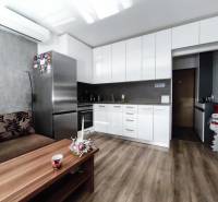 Küche in einer Einzimmerwohnung mit Holzboden, weißen Schränken und einem Sofa.