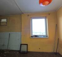 Ein Zimmer in einem Einfamilienhaus mit einem Fenster, einem Besen und orangefarbener Beleuchtung.