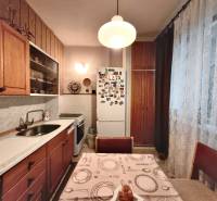 Küche in einer 3-Zimmer-Wohnung mit Holzschränken und Kühlschrank, dekoriert mit Vorhängen.