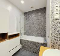 Badezimmer in einer 2-Zimmer-Wohnung mit Badewanne, Mosaikfliesen und Stauraum.