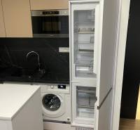 Küche in einer Einzimmerwohnung mit Waschmaschine, Holzboden und offenem Kühlschrank.