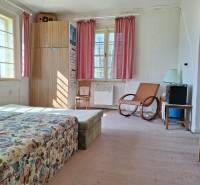 Ein Zimmer mit einem Blumensofa, einem Sessel, einem Schrank und rosa Vorhängen in einem Einfamilienhaus.