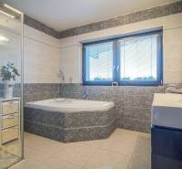 Ein Badezimmer in einem Einfamilienhaus mit Badewanne, Dusche und Waschbecken, helle Fliesen, Fenster mit Rollläden.