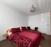 Schlafzimmer mit einem Bett mit gemusterten Bezügen, Deckenleuchte und Kleiderschrank in einer 3-Zimmer-Wohnung.