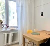 Eine Lampe über einem Holztisch, weiße Vorhänge und Blumendekoration auf der Fensterbank in einer 2-Zimmer-Wohnung.