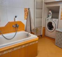 Ein Badezimmer in einem Einfamilienhaus mit einer Badewanne, einem Waschbecken, einer Waschmaschine und gelben Fliesen.