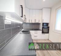 Küche in einer 3-Zimmer-Wohnung mit weißen Schränken, grauer Arbeitsplatte und Bodenbelag in Holzoptik.