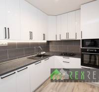 Küche in einer 3-Zimmer-Wohnung mit weißen Schränken und Geräten, Boden mit Holzdekor.