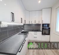 Küche in einer 3-Zimmer-Wohnung mit weißen Schränken und einem Boden in Holzoptik.