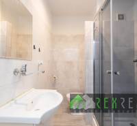 Badezimmer in einer 3-Zimmer-Wohnung mit Duschkabine, Waschbecken und hellen Fliesen.