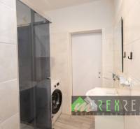 Badezimmer in einer 3-Zimmer-Wohnung mit Duschkabine und Waschmaschine, Fliesen an den Wänden.