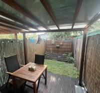 Überdachte Terrasse mit Tisch und Stühlen, umgeben von einem Schilfzaun, Garten mit Pflanzen.