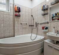 Badezimmer im Einfamilienhaus mit Eckbadewanne, Waschbecken und weißen Fliesen.