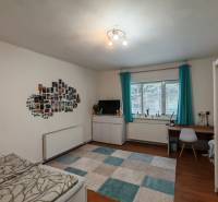 Ein Zimmer in einem Einfamilienhaus mit einem Schreibtisch, einem Bett, Fotos an der Wand und einem Boden in Holzoptik.