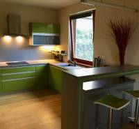 Küche in einem Einfamilienhaus mit grünen Schränken und einer Bar, Boden mit Holzdekor.