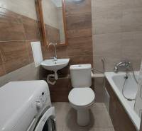 Badezimmer in einer Einzimmerwohnung mit Badewanne, Waschbecken und Waschmaschine, gefliest mit Keramikfliesen.