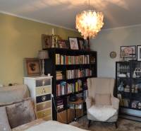 Ein Zimmer in einer 3-Zimmer-Wohnung mit einem Sessel, einem Bücherregal, Kronleuchtern und Dekorationen an den Wänden.
