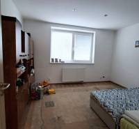 Ein Zimmer in einem Einfamilienhaus mit einem Bett, Möbeln und einem Boden in Holzoptik.