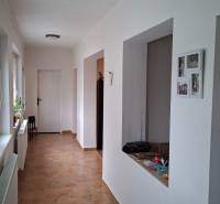 Der Flur eines Einfamilienhauses mit Fliesenboden und weißen Wänden, mit einer offenen Tür auf der rechten Seite.