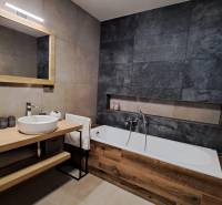 Badezimmer in einer 2-Zimmer-Wohnung mit Badewanne, Spiegel und Waschbecken auf einem Holztisch.