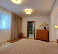 Schlafzimmer in einer 2-Zimmer-Wohnung mit Holzelementen, Vorhängen und hellen Möbeln.