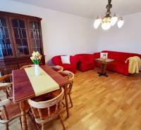 Holzvitrine, rote Sitzgarnitur und Esstisch mit Blumen in einer 4-Zimmer-Wohnung.