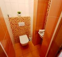 Toilette in einer 4-Zimmer-Wohnung mit orangefarbenen Fliesen und Mosaik, kleines Waschbecken in der Ecke.