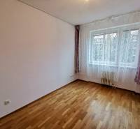 Ein Zimmer mit hellen Wänden, einem Boden mit Holzdekor, einem Fenster mit Vorhängen in einer 4-Zimmer-Wohnung.