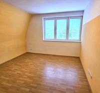 Ein Zimmer mit einem Fenster, gelben Wänden und einem Boden in Holzoptik in einem Gebäude.