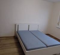 Schlafzimmer in einer Einzimmerwohnung mit Bett, Schrank und Boden in Holzoptik.