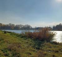 Der Fluss in Mostová, umgeben von landwirtschaftlichen und forstwirtschaftlichen Flächen, die Sonne über dem Horizont.