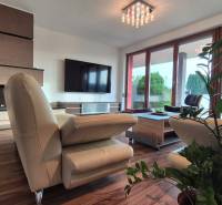 Wohnzimmer eines Einfamilienhauses mit Ledersofa, Kamin, Fernseher und Boden in Holzoptik.