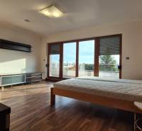 Ein Schlafzimmer in einem Einfamilienhaus mit Holzboden, einem Bett und großen Balkontüren.