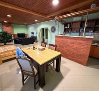 Wohnzimmer eines Einfamilienhauses mit einer Theke aus Ziegelsteinen, einem Essbereich, einem Sofa und einem Boden in Holzoptik.