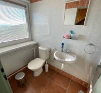 Badezimmer im Einfamilienhaus mit Toilette, Waschbecken, Fliesen und Fenster mit Jalousien.