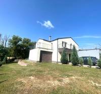 Ein Einfamilienhaus in Melčice-Lieskové mit einem Parkplatz und einem grünen Rasen, umgeben von Bäumen.