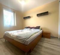 Schlafzimmer im Einfamilienhaus mit Bett, Nachttisch und Boden in Holzoptik.