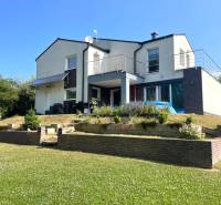 Ein Einfamilienhaus in Melčice-Lieskové mit Garten und Terrasse; Rasenfläche mit Blumen.