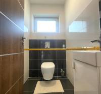 Badezimmer in einem Einfamilienhaus mit Toilette, hellen Wänden und schwarzen Fliesen.