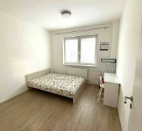 Schlafzimmer mit heller Wand, Bett und Schreibtisch, Boden mit Holzdekor.