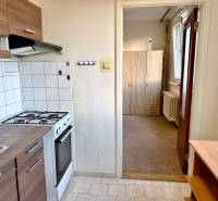 Küche mit weißen Fliesen, Herd, Schränken und Blick in den Flur in einer Einzimmerwohnung.