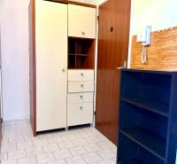 Der Flur einer Einzimmerwohnung mit Fliesen, Schränken und einem Telefon an der Wand.