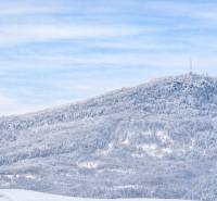 Verschneite Landschaft mit dichtem Wald und einem Sendemast auf einem Hügel bei Banská Štiavnica.