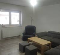 Wohnzimmer in einem Einfamilienhaus mit Sofa, Sessel und Fernseher, Boden mit Holzdekor.