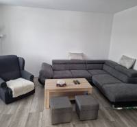 Wohnzimmer in einem Einfamilienhaus mit komfortablem Sofa, Sessel und Boden in Holzoptik.