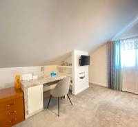 Ein Zimmer in einem Einfamilienhaus mit einem Schreibtisch, einem Fernseher und einem hellen Teppich.