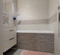 Ein Badezimmer mit Badewanne, grauen Fliesen und einem rosa Teppich in einer 3-Zimmer-Wohnung.