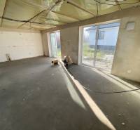 Ein leerer Raum mit großen Fenstern in einem Einfamilienhaus, ohne Bodenbelag.