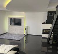 Wohnzimmer in einem Einfamilienhaus mit Treppe, Kamin und Fernseher an der Wand.